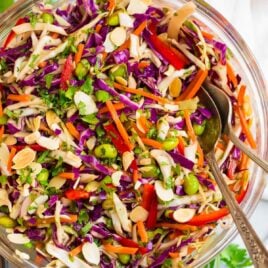 A fresh and healthy Asian Cabbage salad with raw cabbage, almonds, bell pepper and carrots in a ginger peanut dressing in a clear salad bowl