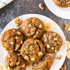 white plate full of healthy banana muffins surrounded by walnut pieces