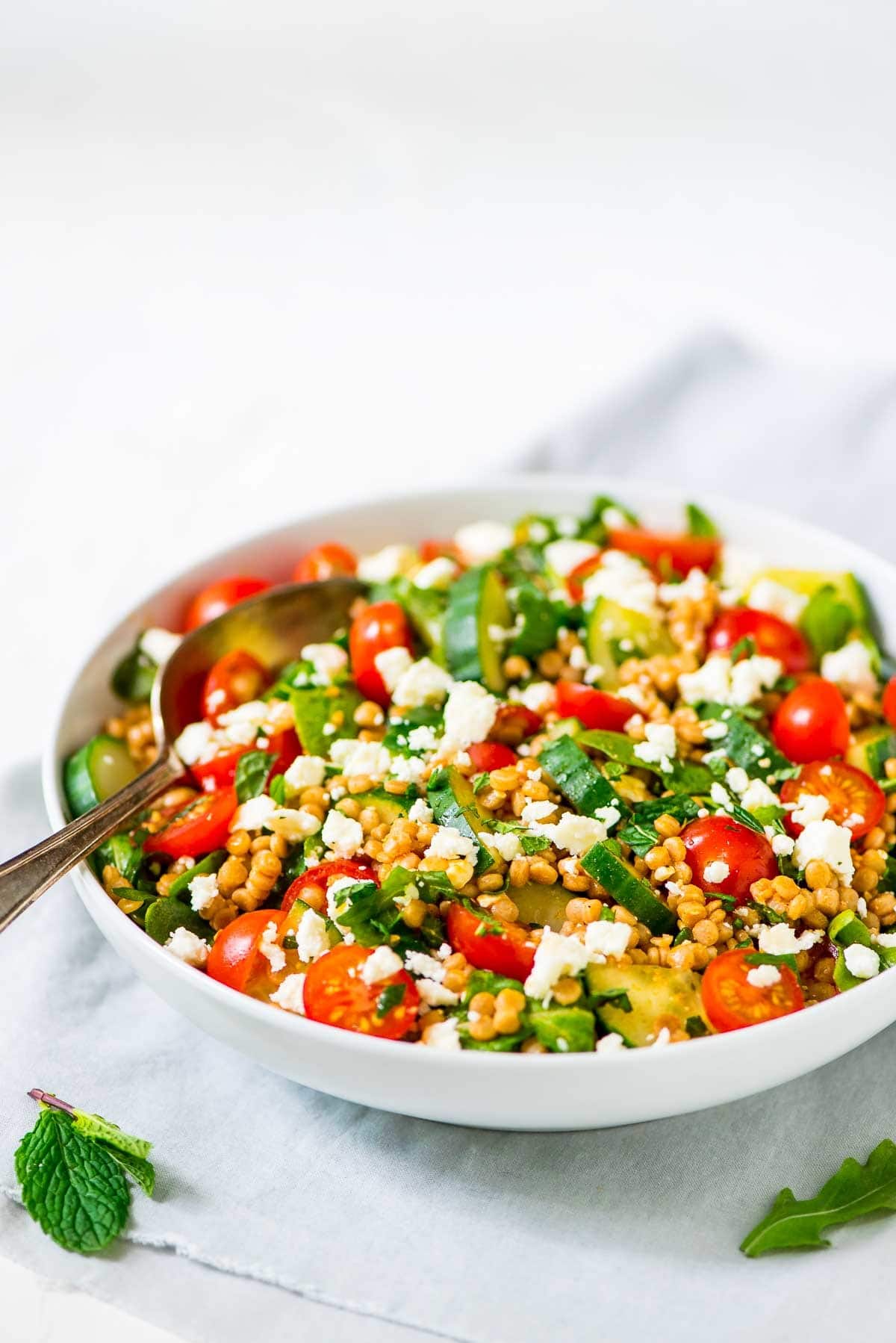 Pearl Couscous Mediterranean Salad with Feta and Mint in a white bowl with a serving spoon