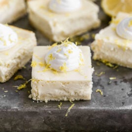 A Lemon Cheesecake Bars with shortbread crust cut into squares and garnished with fresh lemon zest and cream